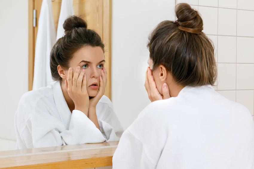 woman looking at tired dull skin in mirror with low glow